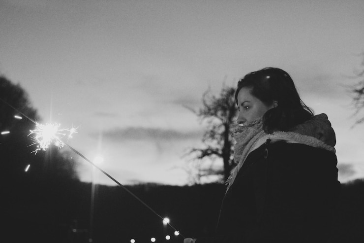 Foto vista lateral de una mujer sosteniendo una chispa mientras está de pie contra el cielo