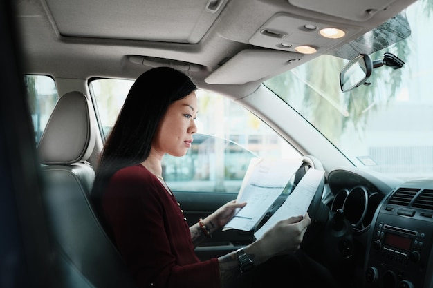 Vista lateral de una mujer sosteniendo documentos mientras está sentada en el coche