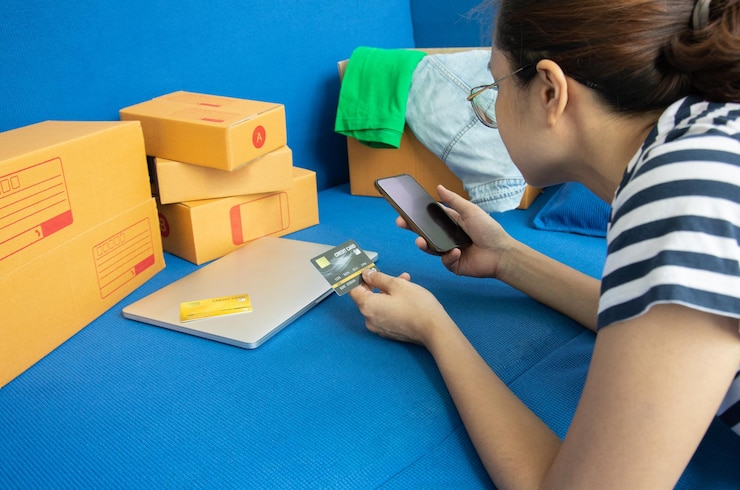 Foto vista lateral de una mujer con una tarjeta de crédito usando un teléfono inteligente mientras está acostada en la cama