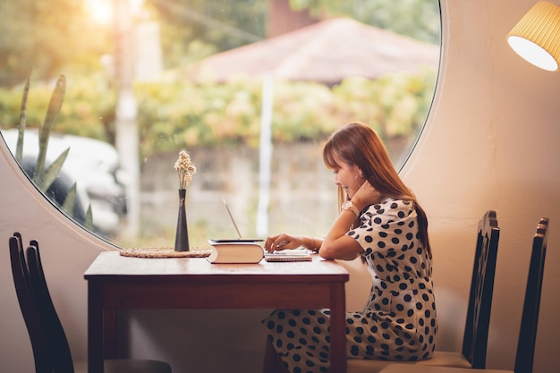 Vista lateral de una mujer usando el teléfono móvil mientras está sentada junto a la ventana en una cafetería