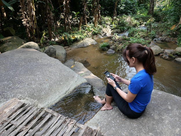 Foto vista lateral de una mujer usando el teléfono móvil mientras está sentada en una roca