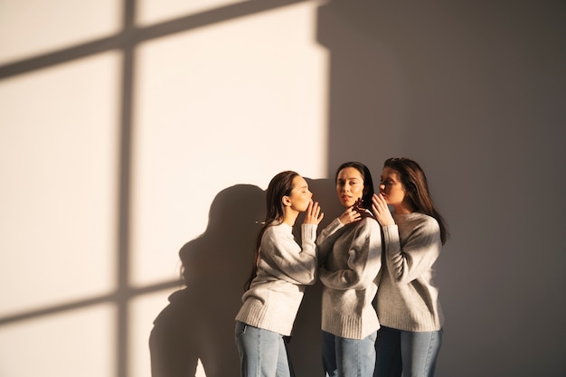 Foto vista lateral de mujeres en suéteres y jeans susurrando entre sí en la sombra de la ventana