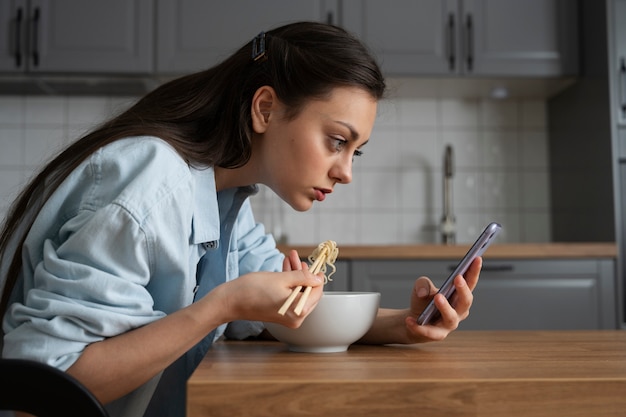 Foto vista lateral mulher comendo com smartphone