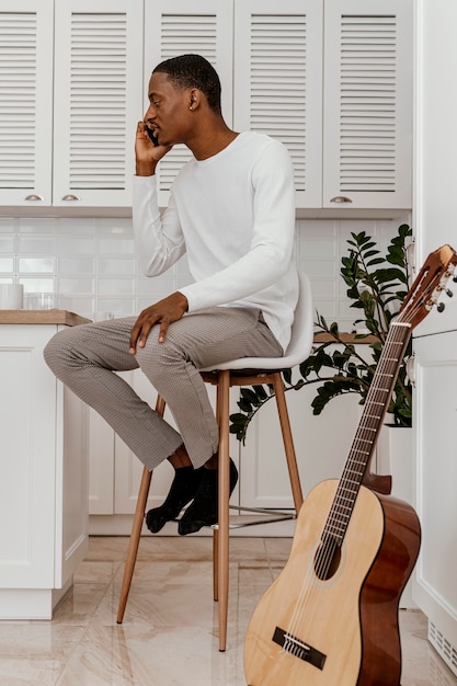 Foto vista lateral del músico masculino hablando por teléfono junto a la guitarra