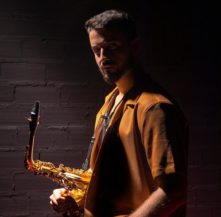 Foto vista lateral del músico posando mientras sostiene el saxofón