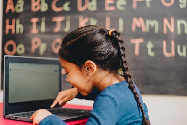 Vista lateral de una niña estudiando en una computadora portátil en casa