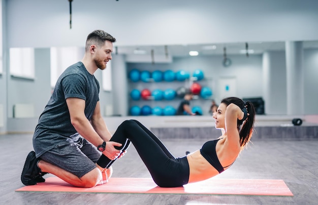 Vista lateral de una niña haciendo ejercicios de prensa en la alfombra con la ayuda de un hombre y una mujer felices sonrientes en buena forma deportiva haciendo ejercicios