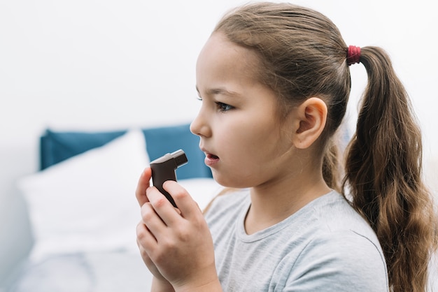 Foto vista lateral de una niña con inhalador de asma en casa