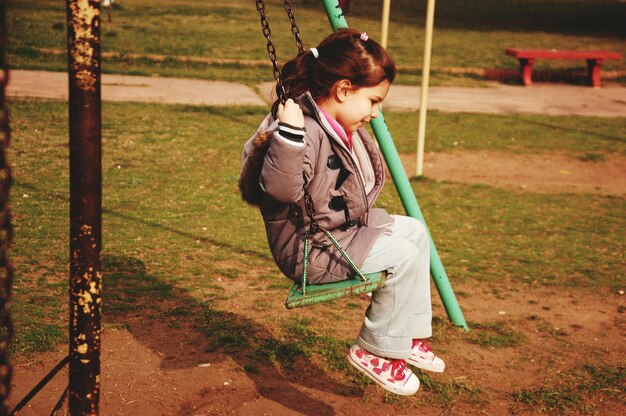 Vista lateral de una niña jugando en el columpio en el parque