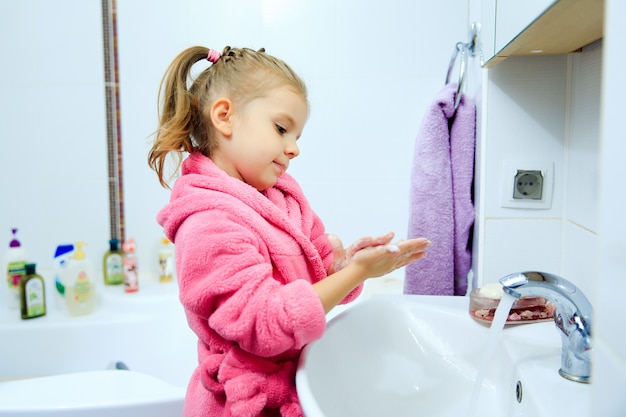 Foto vista lateral de la niña linda con cola de caballo en bata de baño rosa que se lava las manos.