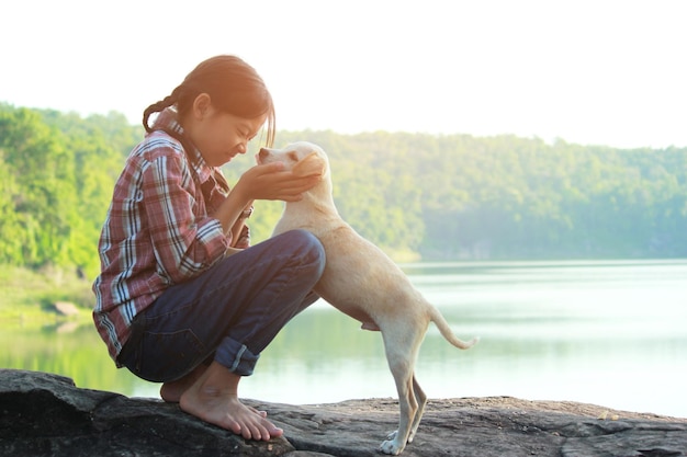 Vista lateral de una niña con un perro en una roca contra el lago