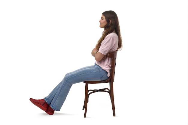 Foto vista lateral de una niña sentada en una silla con los brazos cruzados sobre un fondo blanco