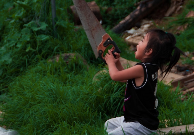 Foto vista lateral de una niña con la sierra en la mano en tierra