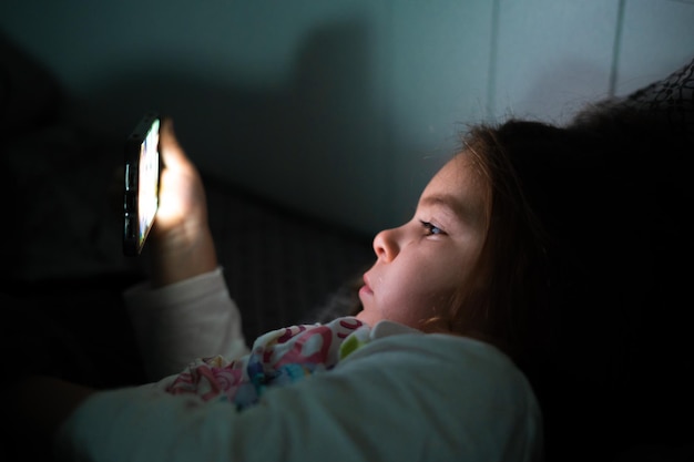 Vista lateral de una niña usando un teléfono inteligente en casa