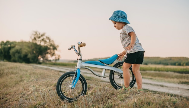 Foto vista lateral de un niño caucásico con bicicleta en el campo cerca de la carretera nacional sombrero azul estilo de vida saludable b ...