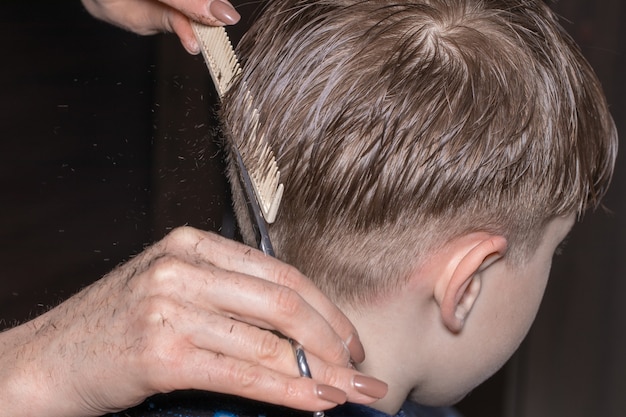 Vista lateral del niño lindo cortarse el pelo por peluquero en la barbería.