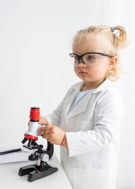 Vista lateral del niño lindo con microscopio y gafas de seguridad