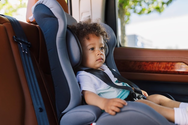 Vista lateral de un niño lindo sentado en un asiento de seguridad para bebés