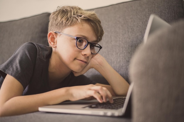 Vista lateral de un niño lindo usando una computadora portátil en el sofá