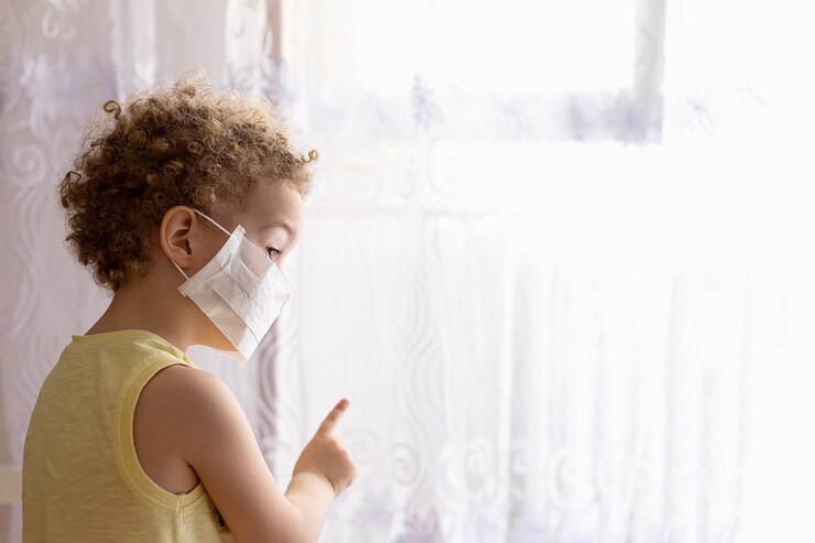 Foto vista lateral de un niño con una máscara de pie junto a la cortina en casa