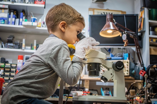 Vista lateral de un niño mirando a través del microscopio en el taller