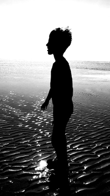 Foto vista lateral de un niño silueta de pie en la orilla en la playa