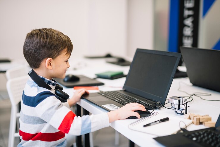 Foto vista lateral de un niño sonriente usando una computadora portátil y un ratón en el aula
