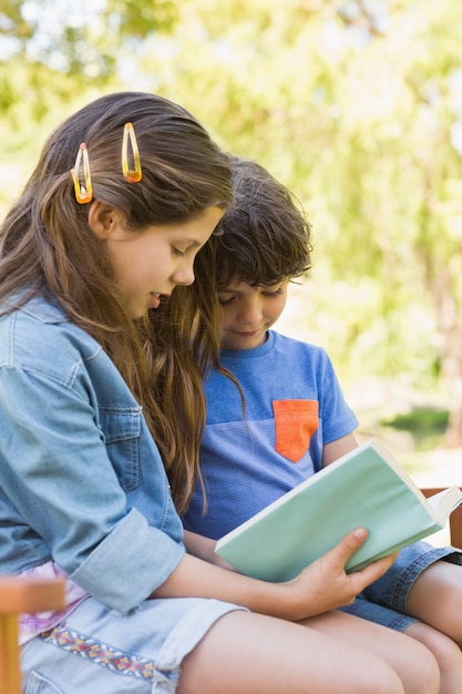 Vista lateral de los niños leyendo el libro en el banco del parque