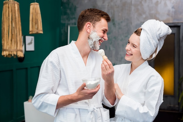 Foto vista lateral de la pareja en batas de baño con espuma de afeitar