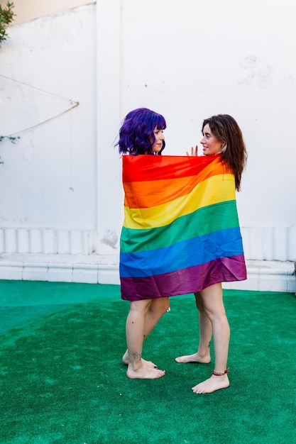 Vista lateral de una pareja de lesbianas usando la bandera del arco iris al aire libre