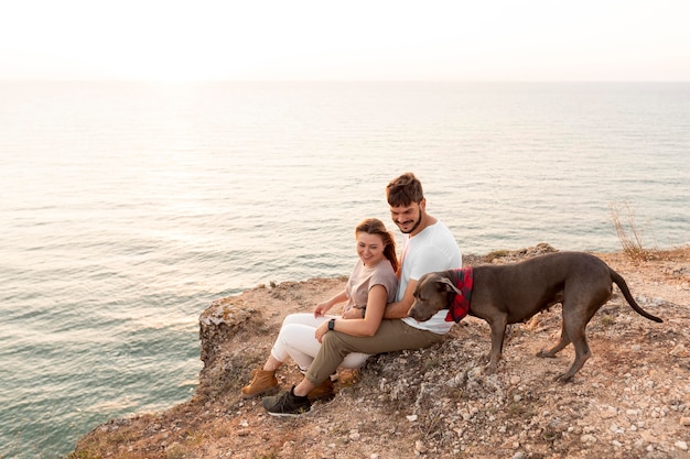 Foto vista lateral de la pareja sentada junto a su perro en una costa