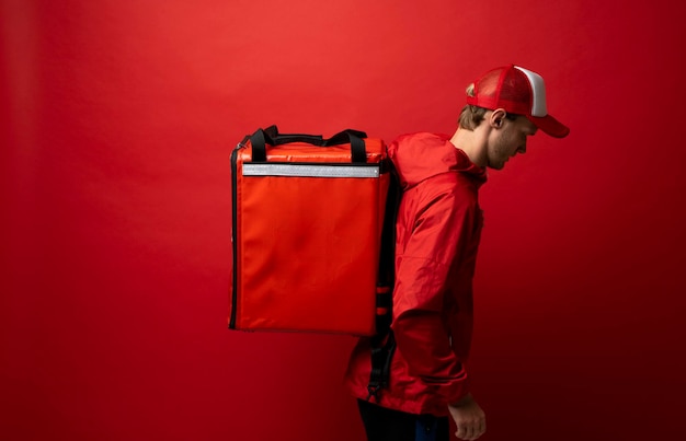 Foto vista lateral de la persona de la entrega que lleva la caja contra un fondo rojo