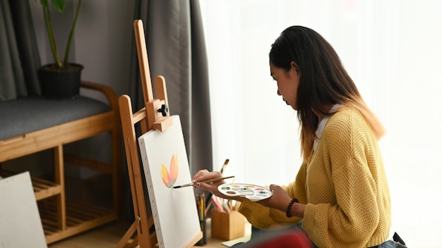 La vista lateral de una pintora está haciendo un dibujo con pintura para carteles en su espacio de trabajo.