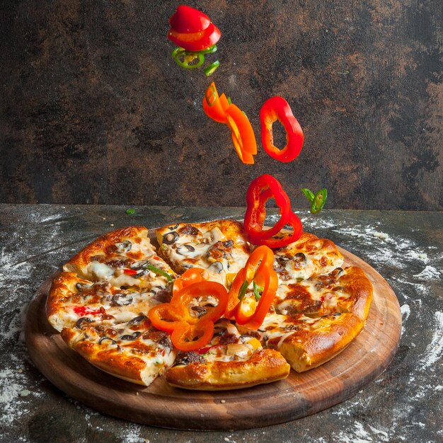 Foto vista lateral de la pizza con rebanadas de pimienta y rebanadas de pizza y harina en utensilios de cocina de tablero sobre fondo de piedra