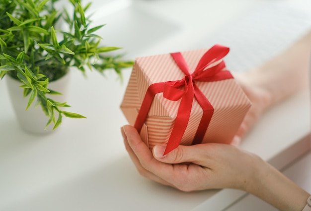 Vista lateral de primer plano de la mano de la mujer sosteniendo una caja de regalo blanca con cinta roja dando presente en el concepto de bonificaciones y sorpresas navideñas