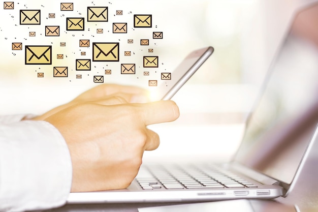 Vista lateral y primer plano de las manos del hombre de negocios usando un teléfono inteligente y una computadora portátil con un boceto de correo electrónico Concepto de marketing por correo electrónico