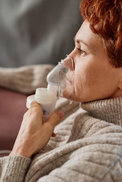 Vista lateral del primer plano vertical de una mujer caucásica madura que tiene coronavirus relajándose en casa usando