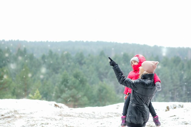 Vista lateral del puesto familiar feliz en el bosque en invierno mujer de mediana edad sosteniendo a una niña apuntando wi