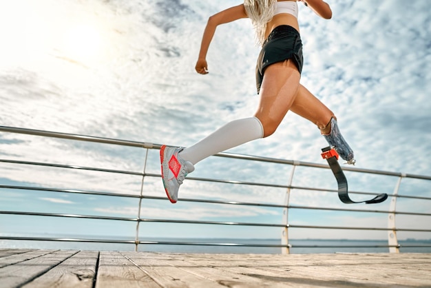 Vista lateral recortada de uma jovem incrível mulher esportiva com deficiência correndo na ponte ao ar livre