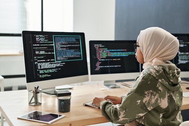 Vista lateral de la red de jóvenes empresarias musulmanas frente a la pantalla de la computadora con información codificada