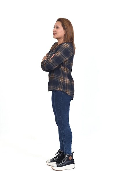 Vista lateral de un retrato completo de una mujer con jeans y zapatillas con los brazos cruzados de fondo blanco.