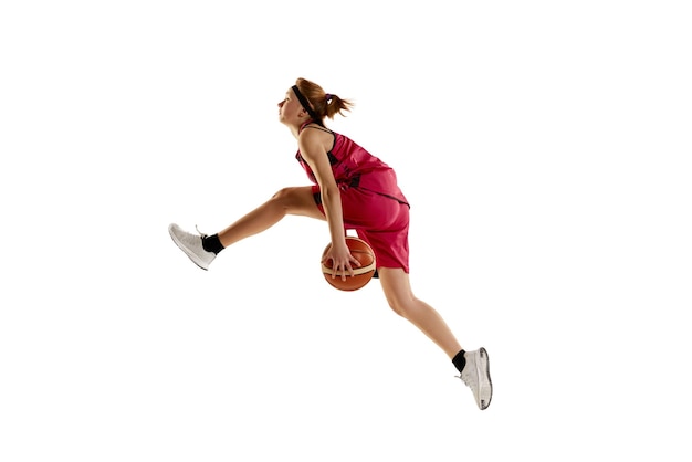 Vista lateral Retrato dinámico de una adolescente jugadora de baloncesto en movimiento en un salto aislado sobre fondo blanco de estudio Concepto de deporte profesional y afición