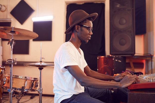 Vista lateral retrato de joven afroamericano escribiendo música en estudio de grabación
