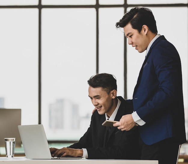 Vista lateral de socios comerciales masculinos asiáticos que navegan por la tableta en la oficina mientras trabajan en un nuevo proyecto