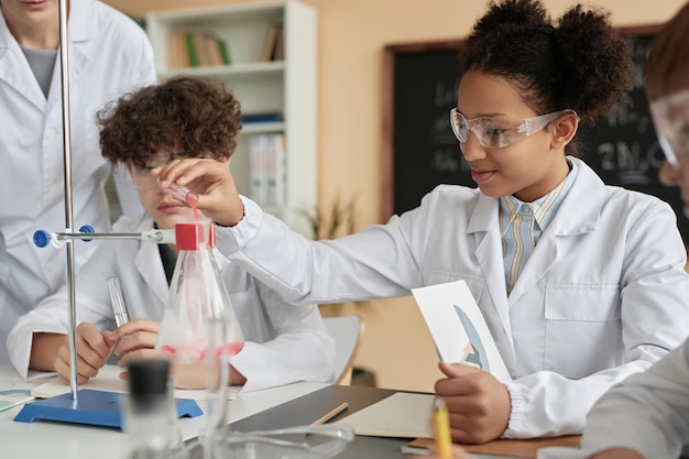 Vista lateral sonriente colegiala negra haciendo experimento científico en la escuela