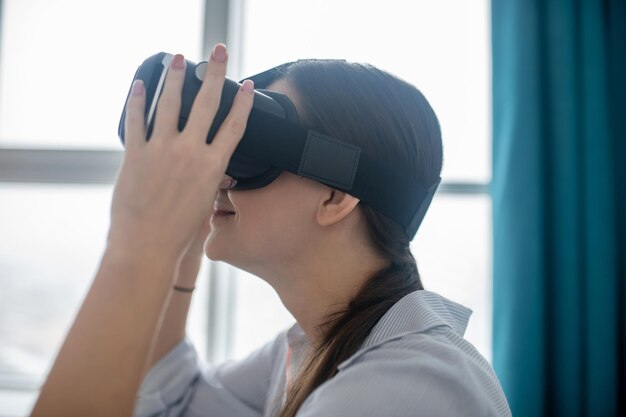 Vista lateral de una sonriente mujer complacida en las gafas VR sumergiéndose en la realidad virtual