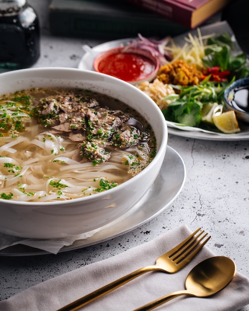 Vista lateral de la sopa pho bo vietnamita con fideos de carne y arroz en la mesa servida