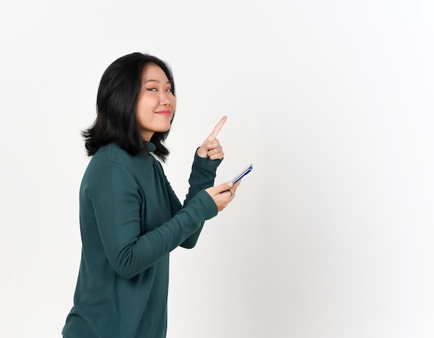 Vista lateral sosteniendo el teléfono inteligente y apuntando al lado Copia el espacio de una hermosa mujer asiática aislada sobre un fondo blanco