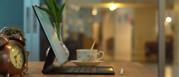 Vista lateral de la tableta digital con teclado, taza de café y decoración en la sala de la oficina en casa