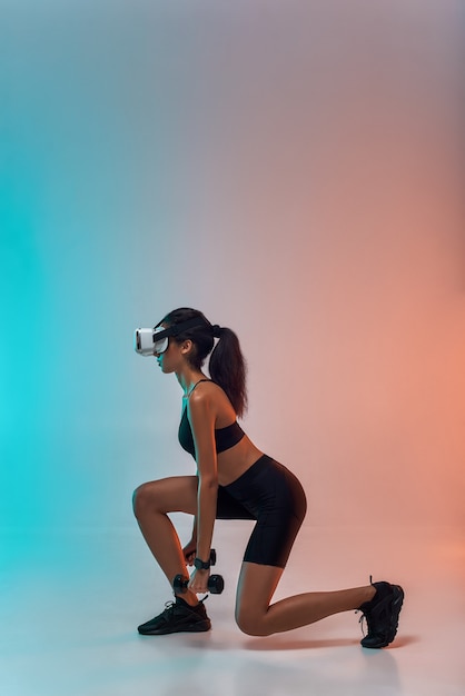 Vista lateral de la tecnología futura de la joven mujer deportiva en ropa deportiva haciendo ejercicio con pesas mientras